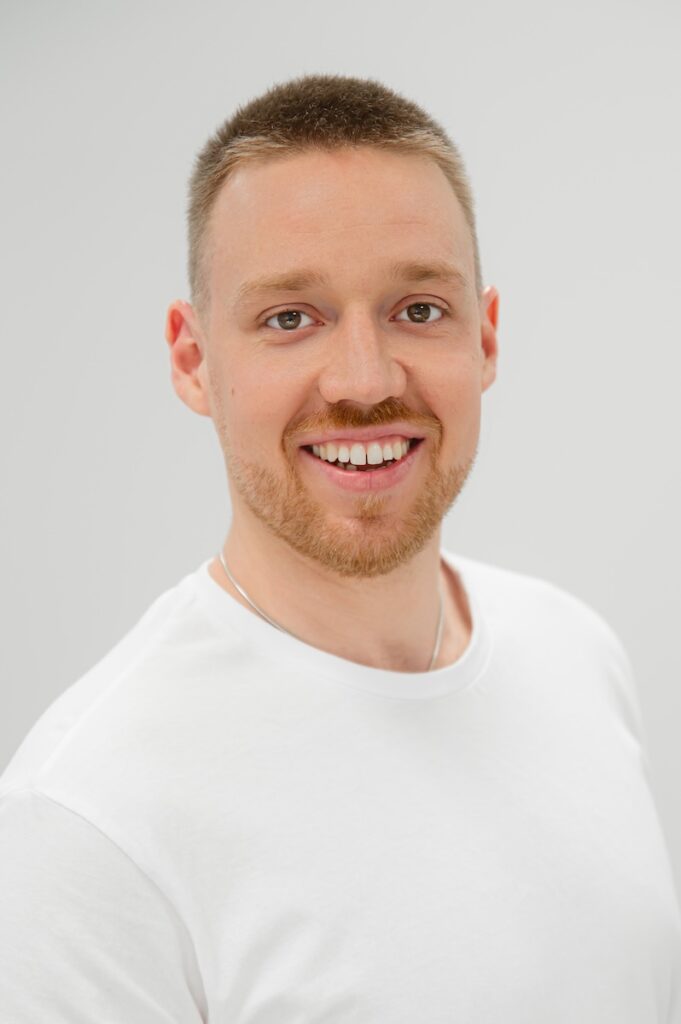 Portraitfoto von Johannes Weigl, Physiotherapeut mit im Therapiezentrum Pro, mit kurzem Haar und Bart in weißem T-Shirt.
