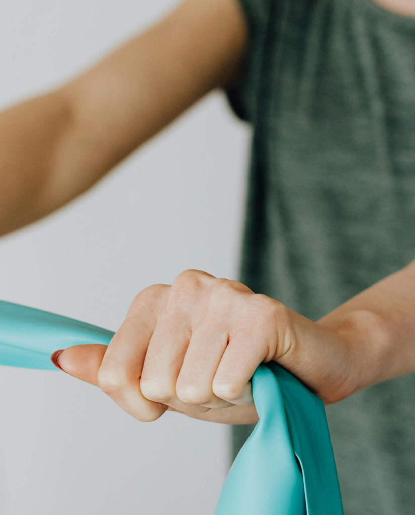 Person hält ein türkisfarbenes Theraband bei einer Physiotherapie-Übung im Therapiezentrum Vitanium Health Solutions