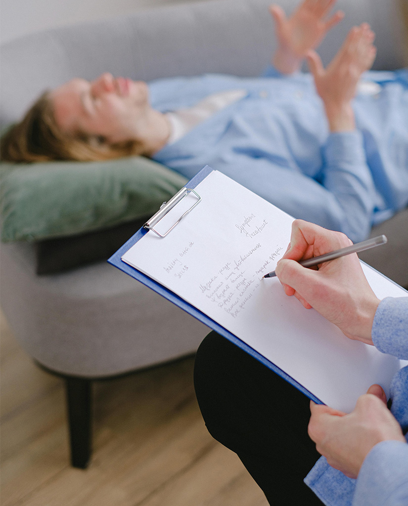 Patient liegt auf Therapiecouch und spricht mit Therapeutin, die Notizen auf Klemmbrett macht – Psychotherapie bei Vitanium Health Solutions