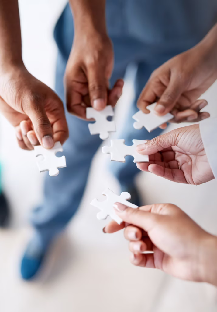 Vier Hände fügen weiße Puzzleteile zusammen – Symbol für passende Therapie bei Vitanium Health Solutions